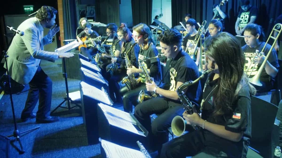 Músicos jóvenes de la Conchalí Big Band tocando saxofones y trombones en un escenario