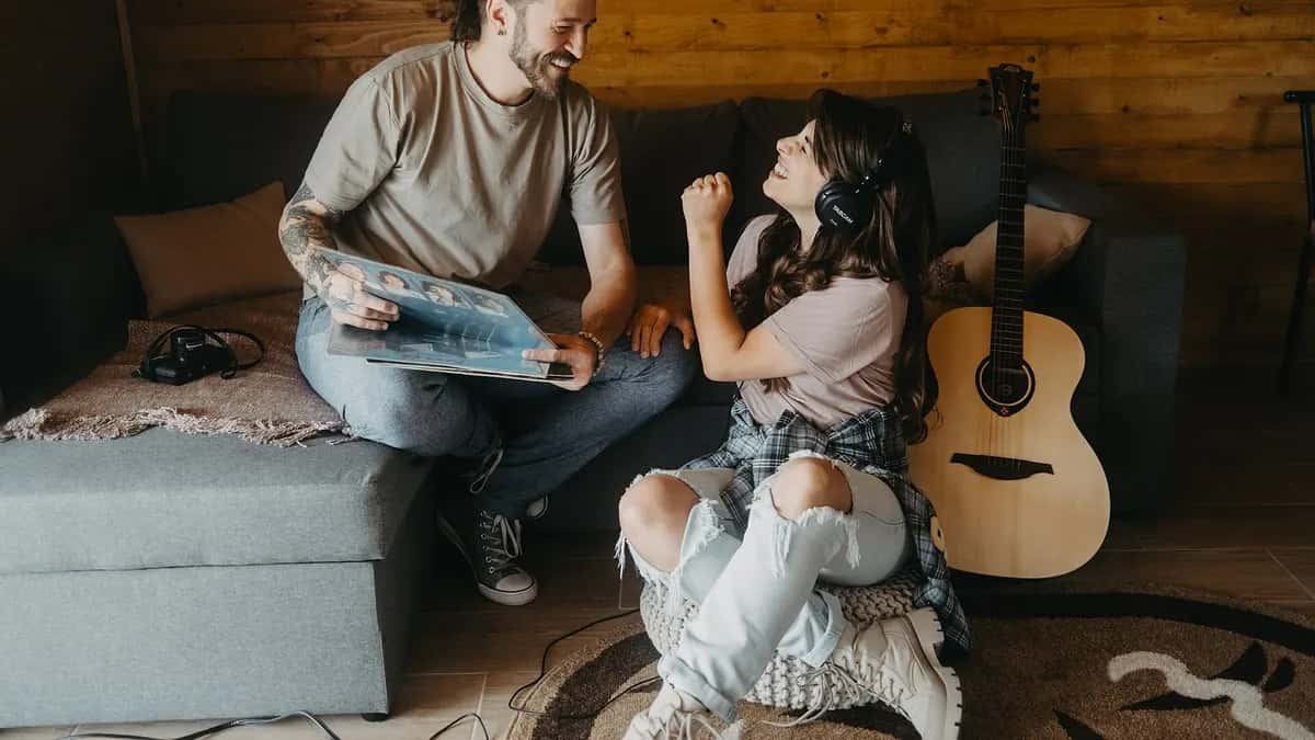 Dos amigos escuchan música en un sillón, uno con audífonos y otro mirando un disco