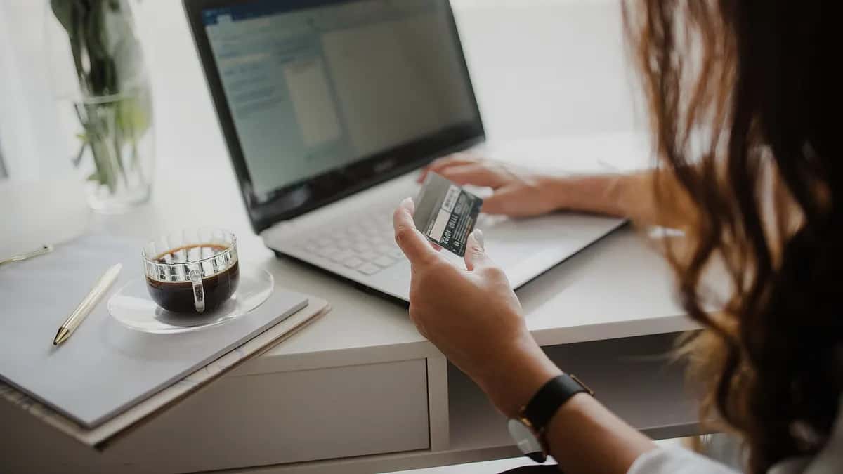 Mulher olhando um cartão de crédito diante do computador
