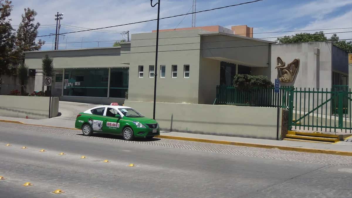 Fachada de uma Unidade de Medicina Familiar do IMSS com um táxi estacionado