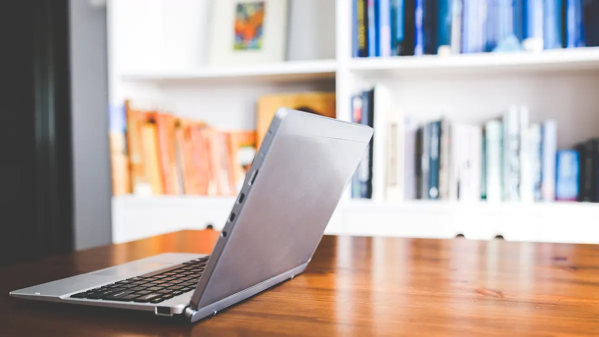 Computador portátil sobre un escritorio de madera frente a una biblioteca